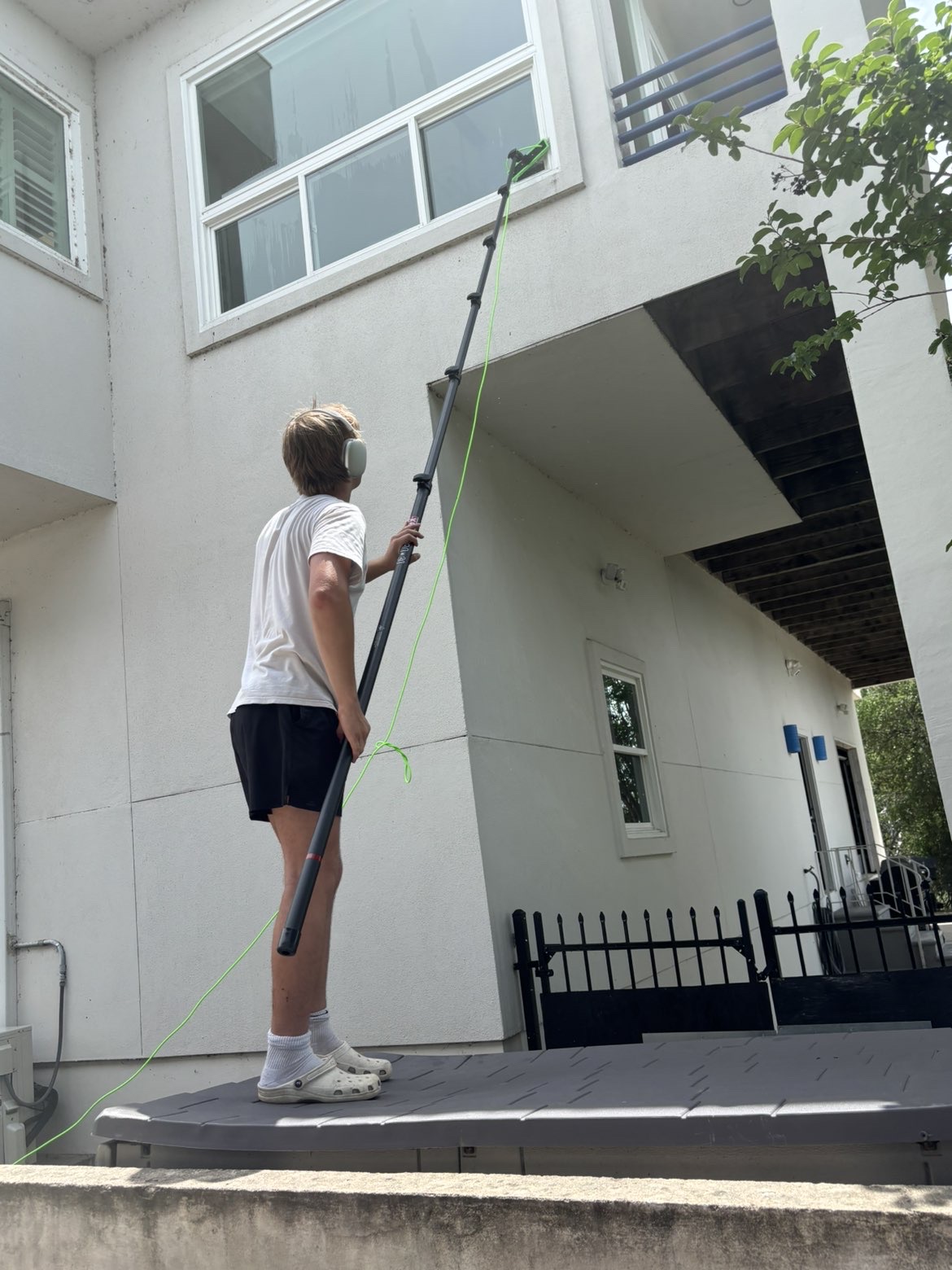 Precise Panes technician reaching second-story windows on a modern white luxury home with a pure-water pole