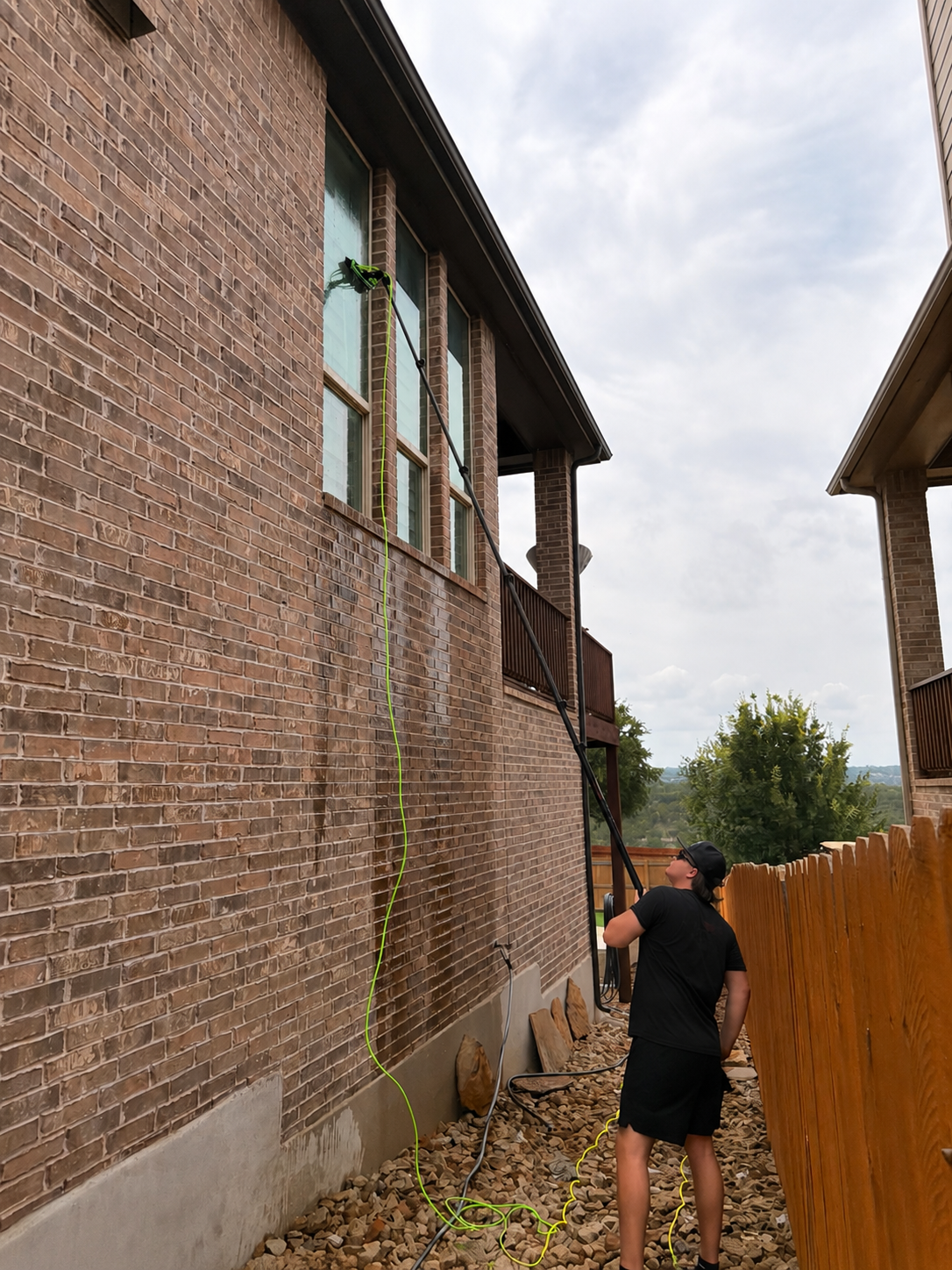 Precise Panes technician using a pure-water pole on a multi-story brick home in Austin, TX