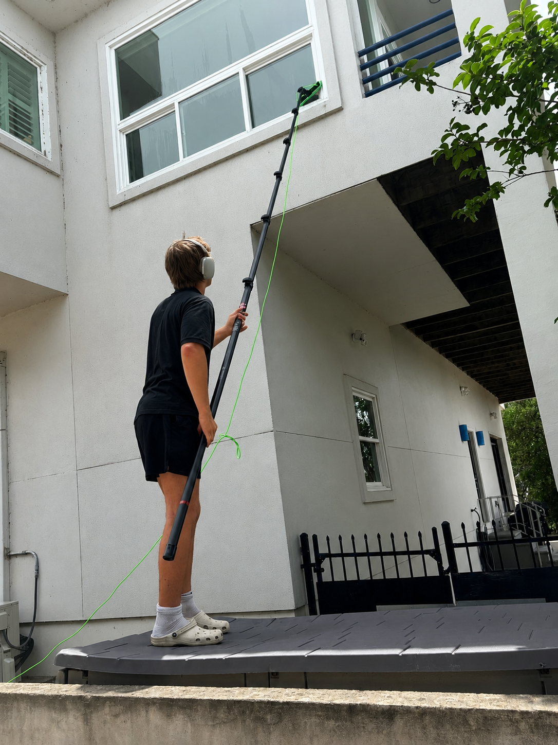 Precise Panes technician reaching second-story windows on a modern white luxury home with a pure-water pole